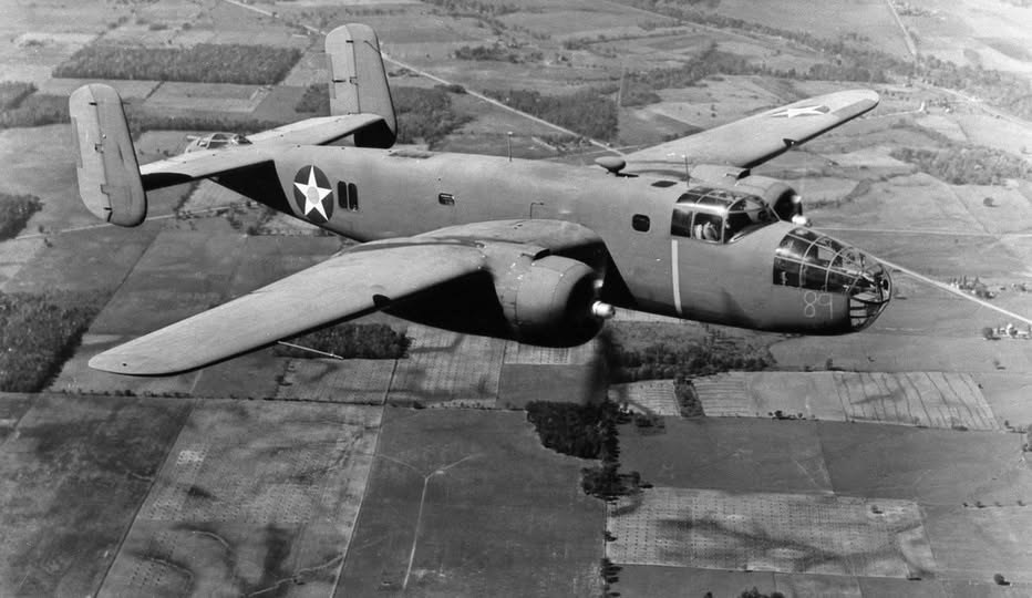 A B-25 Mitchell bomber banking over farm fields, with the number 89 on its nose