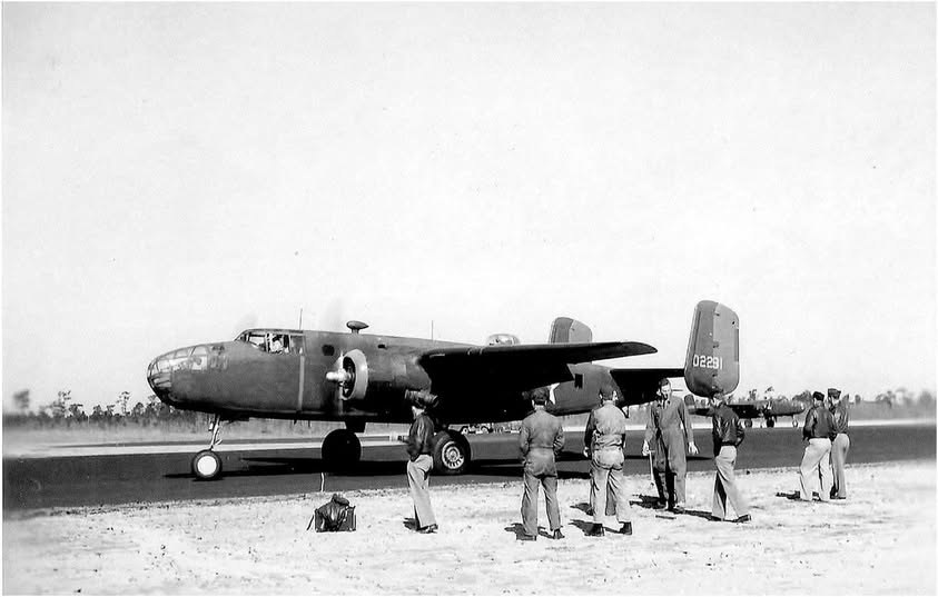 A North American B-25B Mitchell bomber on a runway with tail number 02291 while airmen stand in front of it