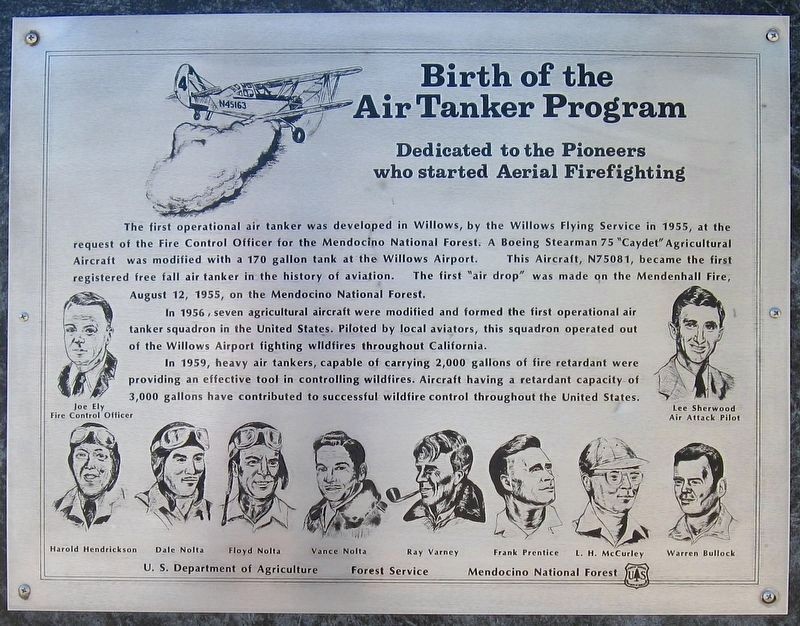 A metal plaque titled Birth of the Air Tanker Program with a drawing of a Stearman biplane dropping water, and line portraits of Joe Ely, Lee Sherwood, and the eight original pilots