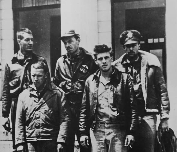 Five members of Doolittle Raid Crew 16 in flight jackets standing in front of a building, three in the back row and two in front